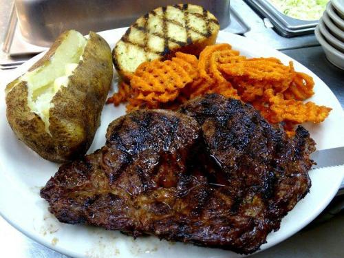 A plate featuring a grilled steak, baked potato, and sweet potato fries, with a slice of grilled bread.