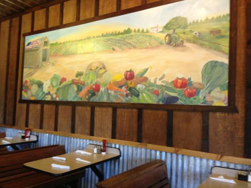 A mural depicting a farm scene with vegetables and a tractor, set in a rustic dining area with wooden tables.