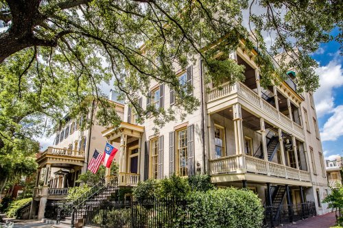 Historic building with balconies, surrounded by greenery, featuring American and state flags under a blue sky.