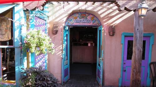Colorful entrance to "The Shed" restaurant, featuring vibrant doors and hanging flowers in a charming outdoor setting.