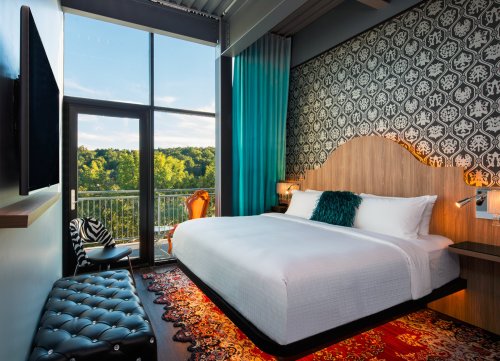Modern hotel room with a large bed, stylish decor, and a balcony overlooking a scenic view.
