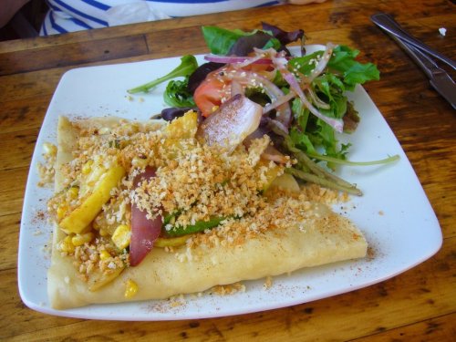 A plate with a savory crepe topped with vegetables and breadcrumbs, accompanied by a fresh salad.