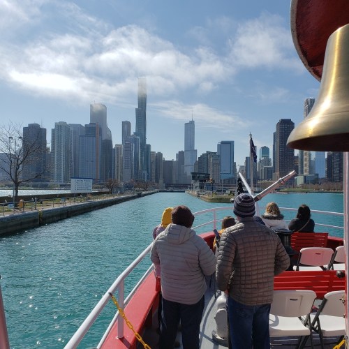 View from a boat on a bright day, showcasing Chicago's skyline with people enjoying the ride.