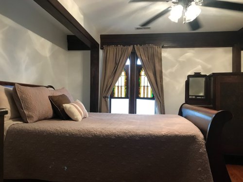 Cozy bedroom featuring a wooden sleigh bed, decorative pillows, and stained glass windows. Soft lighting enhances the ambiance.