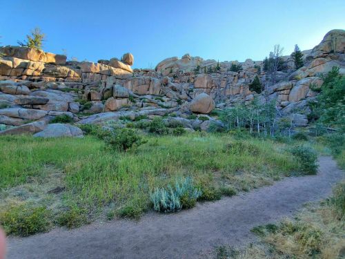 Rocky hillside with large boulders, green grass, and a dirt path leading through a natural landscape.
