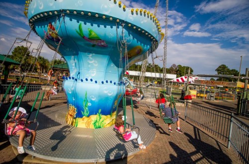 Children enjoy a colorful swing ride at an amusement park on a sunny day.