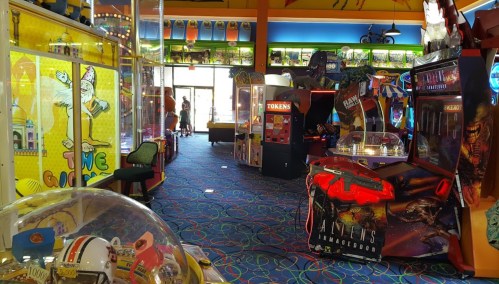 A colorful arcade filled with various games, machines, and bright decor, with people playing in the background.