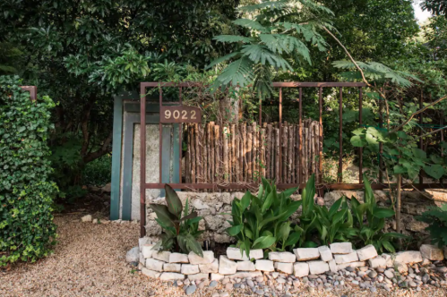 A rustic entrance gate with the number 9022, surrounded by greenery and decorative stones.