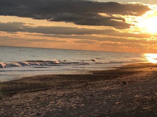 A serene beach at sunset, with gentle waves lapping at the shore and clouds illuminated by warm golden light.