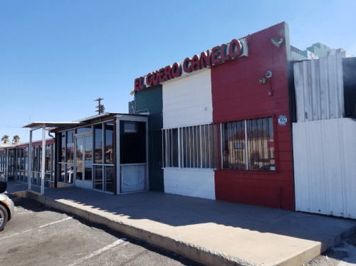 Exterior of El Guero Canelo restaurant, featuring a red, white, and green color scheme, with a clear blue sky above.