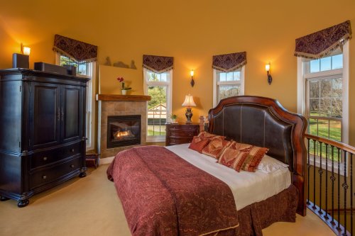 Cozy bedroom with a large bed, elegant decor, a fireplace, and windows overlooking a scenic view.
