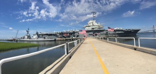 A panoramic view of a naval ship docked at a pier, with American flags and a clear blue sky in the background.