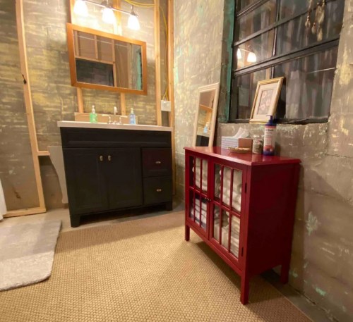 A bathroom with a black vanity, a red cabinet, and a large mirror, featuring a textured wall and soft lighting.