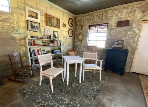 Cozy room with a small table, two chairs, bookshelves, and rustic decor against a textured wall.