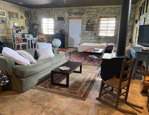Cozy living space with a sofa, chairs, coffee table, and rustic decor, featuring exposed stone walls and natural light.