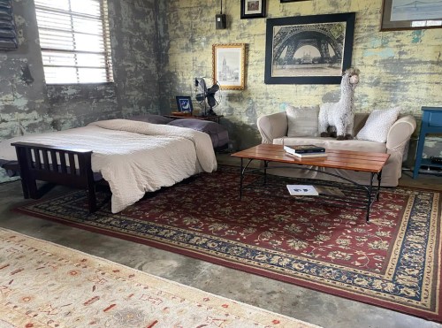 Cozy room with a bed, sofa, wooden coffee table, and decorative wall art in a rustic setting.