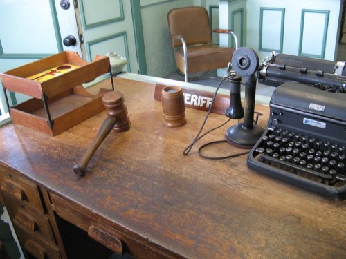 A wooden desk with a typewriter, gavel, and sheriff's sign, set in a vintage office environment.