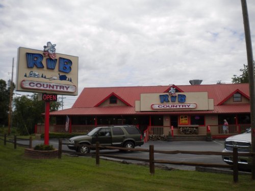 A restaurant named "Rib Country" with a red roof and sign, featuring a grassy area and parked cars outside.