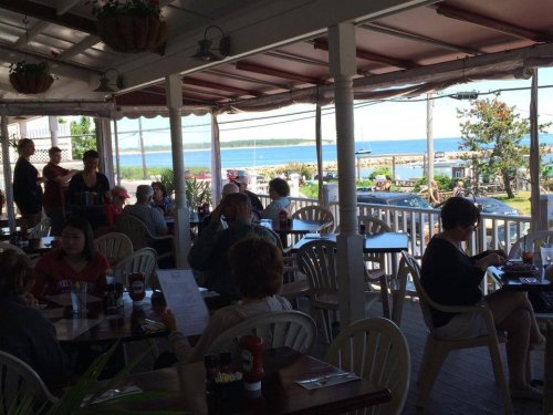 A bustling restaurant with diners enjoying meals, overlooking a scenic waterfront view.