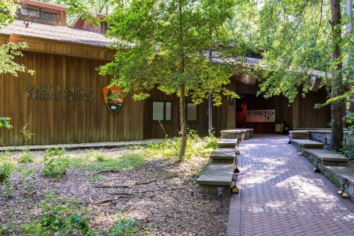 A wooden visitor center surrounded by trees, with a brick pathway leading to the entrance.