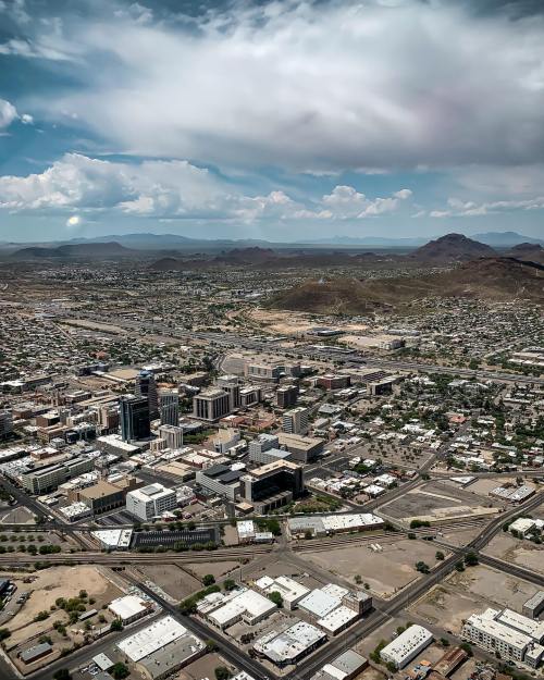 Aerial view of a city with skyscrapers, roads, and mountains in the background under a partly cloudy sky.