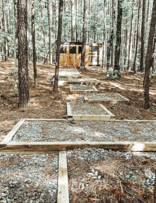 A wooded area with a gravel path leading to a small wooden structure among tall trees.