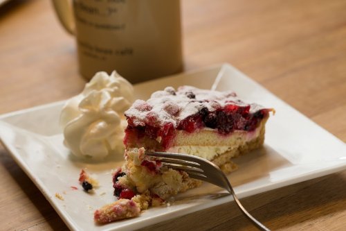 A slice of berry cheesecake topped with powdered sugar, served with a dollop of whipped cream on a white plate.