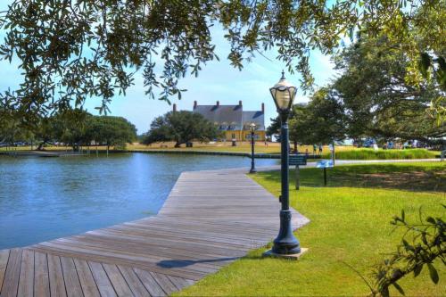 A scenic view of a wooden walkway by a calm pond, with a historic building and trees in the background.