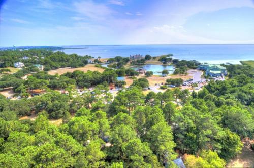 Aerial view of a coastal area with lush greenery, a pond, and buildings near the water under a clear blue sky.