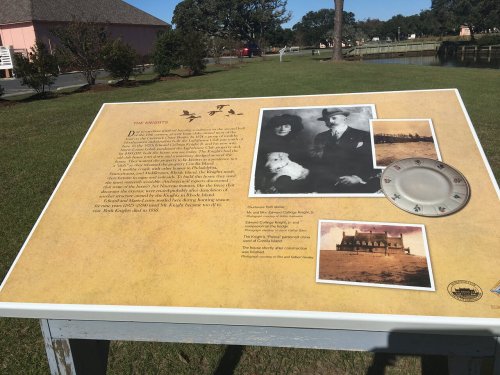 Informational display featuring a historical narrative, photos, and a clock, set in a grassy area near a building.