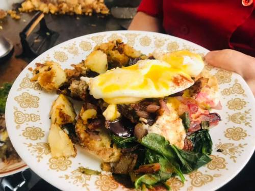 A plate of mixed breakfast featuring potatoes, greens, and two poached eggs, garnished with a golden yolk.