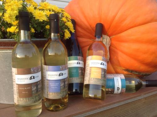 Five bottles of wine from Majestic Oak Winery are displayed next to a large pumpkin and yellow flowers.
