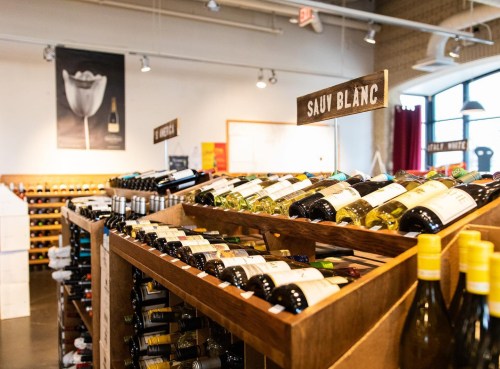A wine shop interior featuring shelves of wine bottles labeled with different varieties, including Sauvignon Blanc.