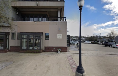 Exterior view of a building with a sign, parking area, and a lamppost under a partly cloudy sky.