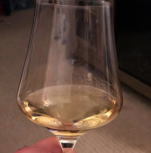 A close-up of a hand holding a wine glass filled with light-colored wine, with a blurred background.