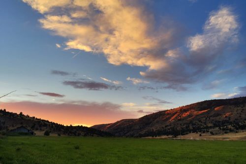 A serene landscape featuring rolling hills, a grassy field, and a colorful sunset sky with scattered clouds.