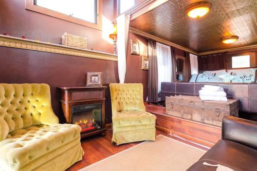 Cozy interior featuring two green velvet chairs, a fireplace, and a bed with decorative pillows in a warm-toned room.
