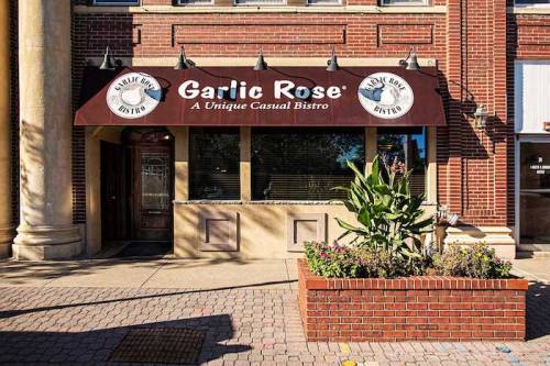 Exterior of Garlic Rose Bistro, featuring a brick facade, large windows, and a planter with greenery.