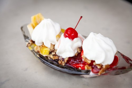 A glass dish filled with ice cream, whipped cream, cherries, nuts, and fruit, served as a colorful dessert.