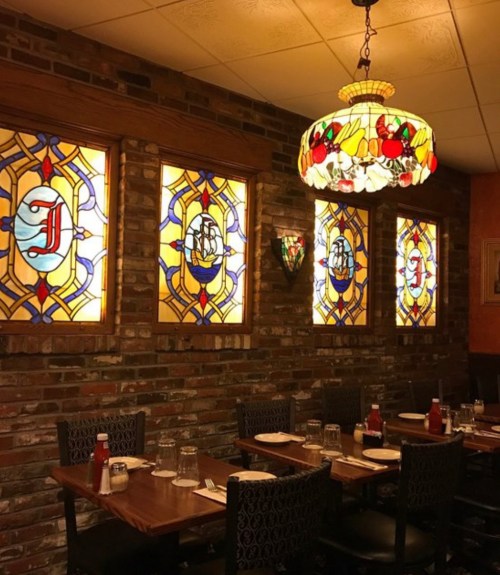Cozy restaurant interior featuring stained glass windows, wooden tables, and a colorful hanging lamp.