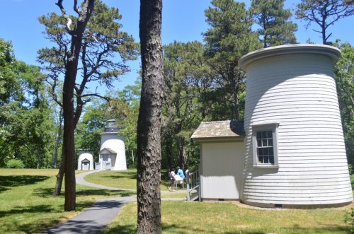 Two white, round buildings surrounded by trees and a grassy path, with people walking in the distance on a sunny day.