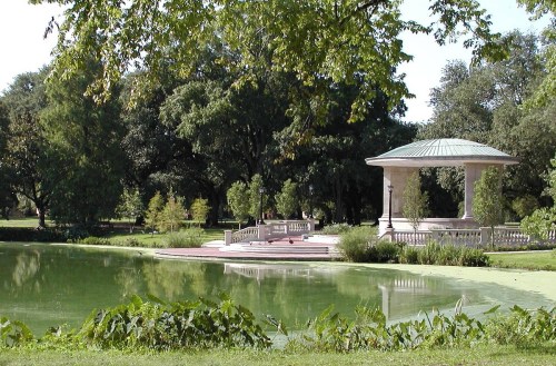 A serene park scene featuring a gazebo by a pond surrounded by lush greenery and trees.