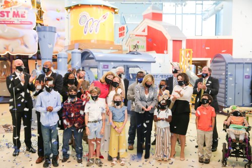 A group of adults and children celebrate with confetti at a festive event in a colorful indoor space.