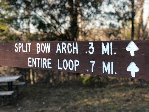 Wooden signpost indicating trail distances: "Split Bow Arch 0.3 mi" and "Entire Loop 0.7 mi," with directional arrows.