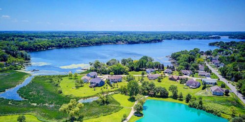 Aerial view of a serene lake surrounded by lush greenery and residential homes on a sunny day.