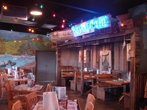 Cozy restaurant interior with wooden decor, colorful string lights, and a vibrant mural of a lakeside scene.