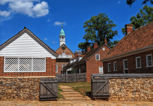 Historic buildings with a stone pathway, a clock tower in the background, under a clear blue sky.