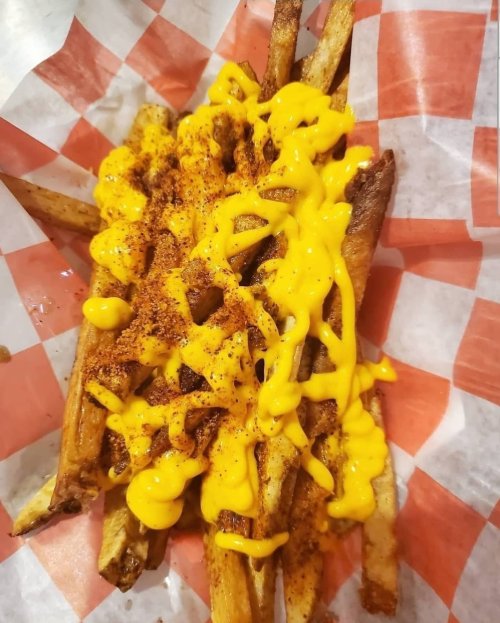 A serving of crispy fries topped with melted cheese and a sprinkle of seasoning, served in a red and white checkered paper.