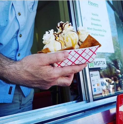 A hand holds a waffle bowl filled with ice cream, topped with whipped cream and drizzled with chocolate sauce.