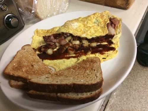 A plate with a bacon and potato omelette drizzled with barbecue sauce, accompanied by three slices of toasted bread.